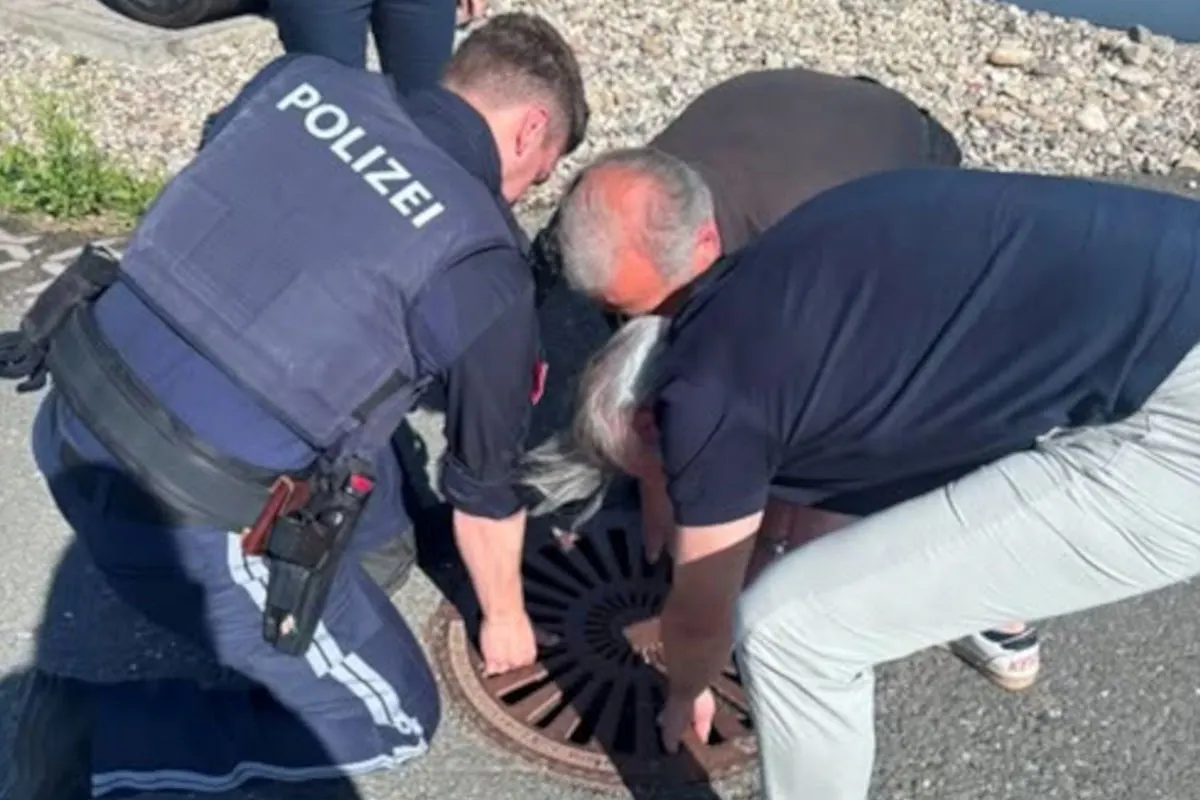 Ein Polizist und zwei zivile Männer arbeiten zusammen, um einen Gullydeckel anzuheben, möglicherweise im Rahmen einer Ermittlung.