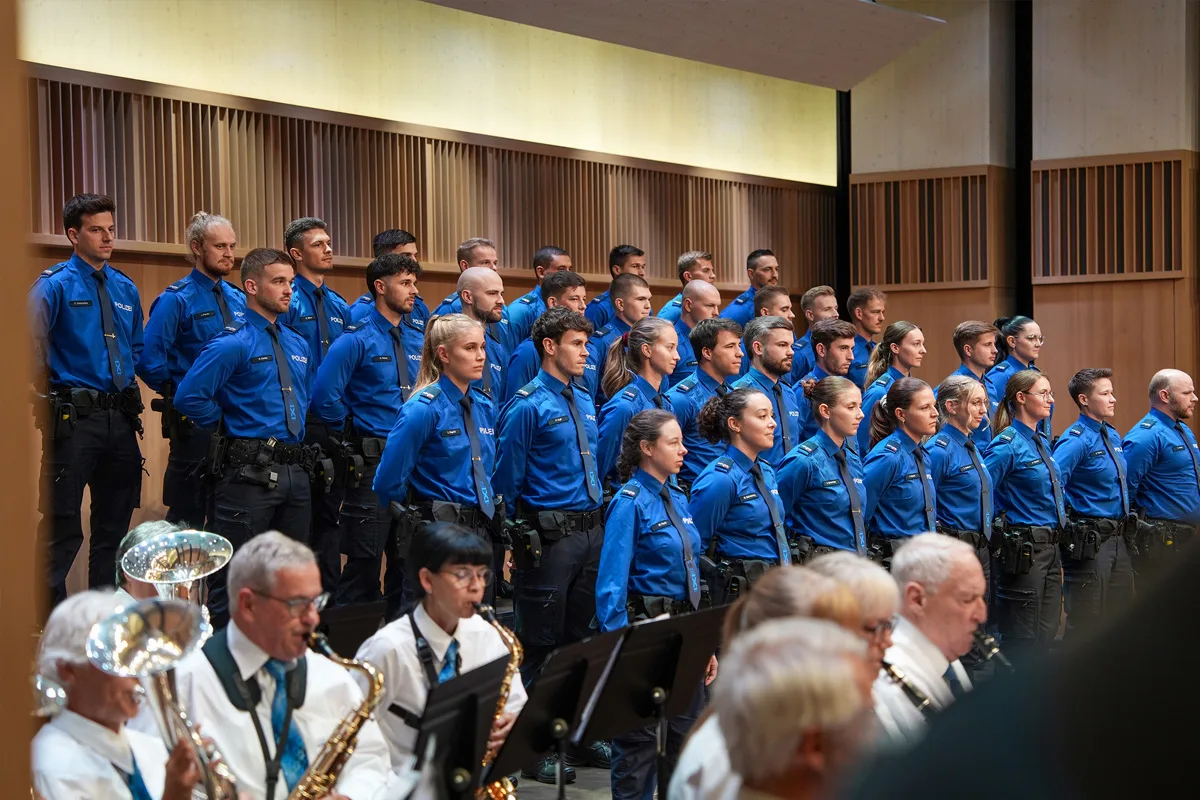 Eine große Gruppe von Personen in blauen Polizei-Uniformen steht in einem Raum. Im Vordergrund sind Musiker mit Blasinstrumenten zu sehen.