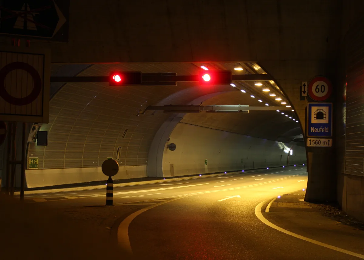 Der Tunnel von Neufeld ist durch eine rote Verkehrsampel blockiert. An den Wänden sind Verkehrsschilder und Beleuchtungen sichtbar.