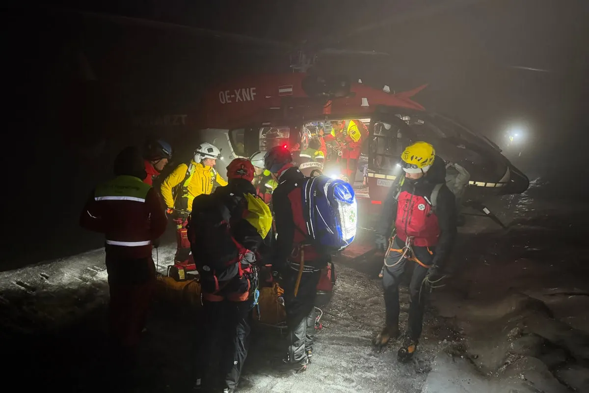 Mehrere Rettungskräfte in Sicherheitskleidung sind bei einem nächtlichen Einsatz um einen Hubschrauber versammelt. Nebel umhüllt die Szene.