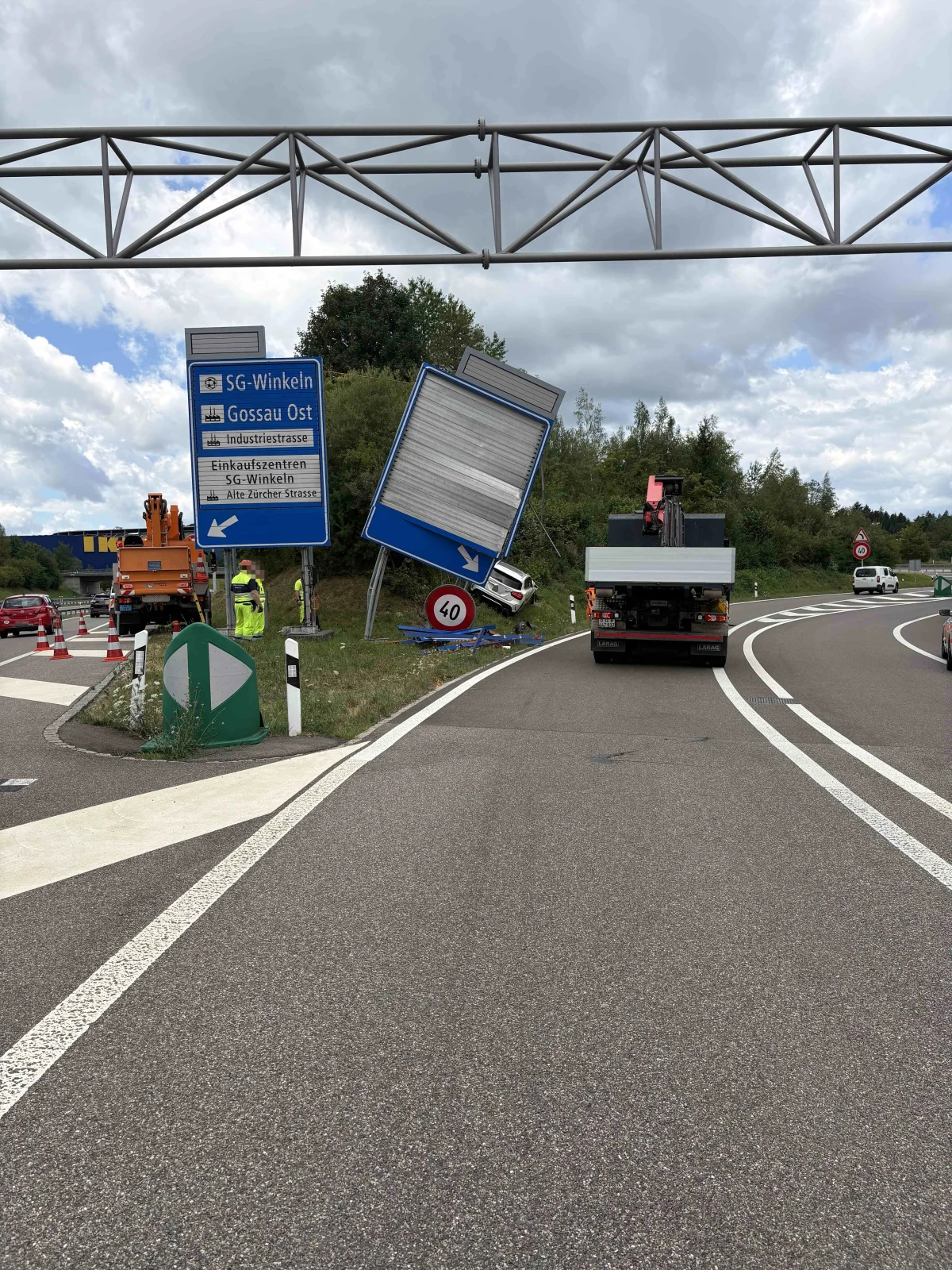 Ein Verkehrsschild ist neben der Straße umgeknickt. Ein Lastwagen steht im Vordergrund. Im Hintergrund sind weitere Schilder und Bäume zu sehen.