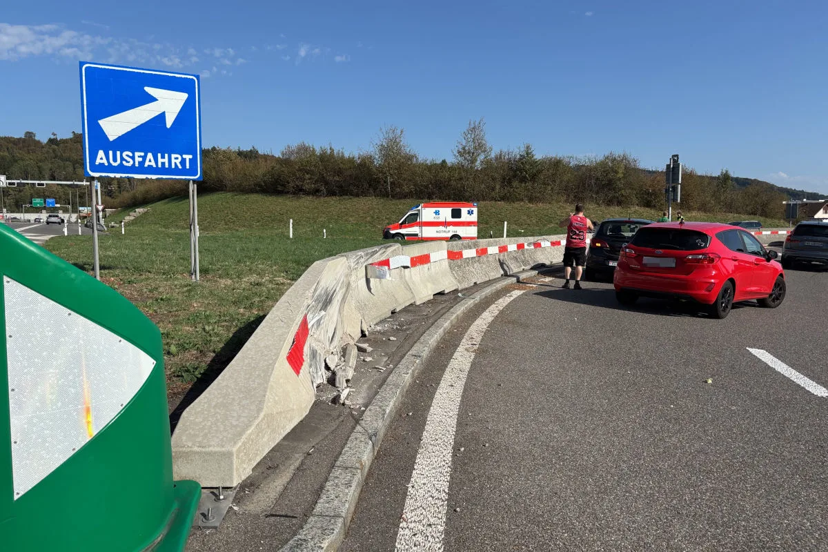 Eine stark beschädigte Leitplanke an einer Autobahnausfahrt, daneben steht ein Rettungswagen und ein geparktes rotes Auto.