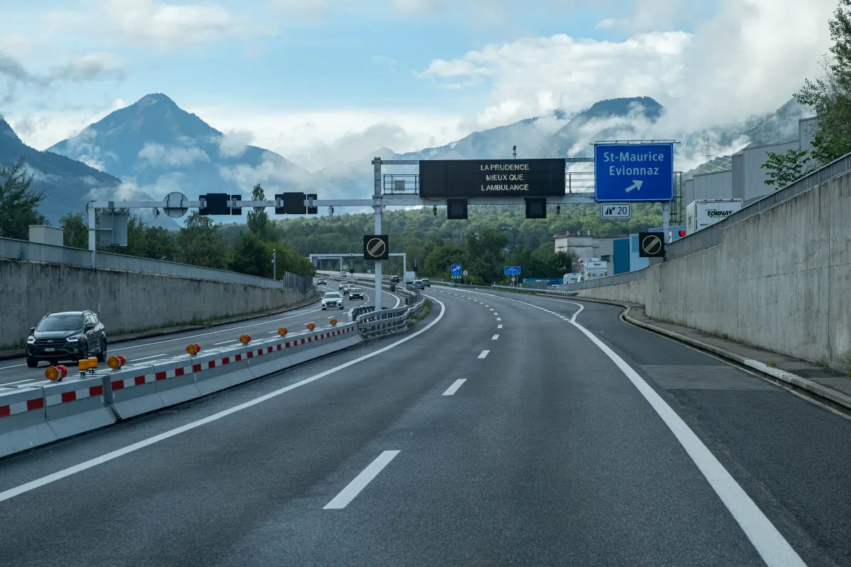 Eine leere Autobahn führt durch eine bergige Landschaft. Verkehrszeichen für St-Maurice und Evionnaz sind sichtbar.
