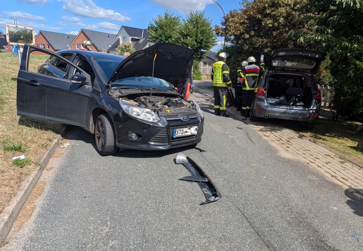 Zwei beschädigte Autos stehen auf einer Straße. Feuerwehrkräfte sind bei einem der Fahrzeuge anwesend.