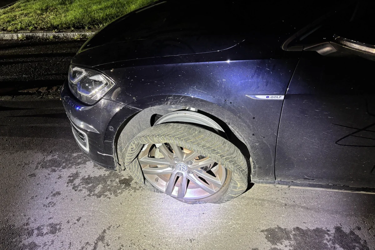 Ein dunkler VW e-Golf steht mit einem stark beschädigten Vorderreifen am Straßenrand. Es ist Nacht und der Reifen ist von der Felge gelöst.