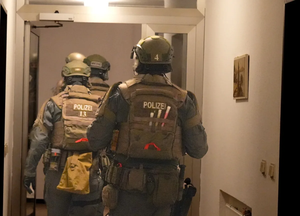 Drei Polizisten in taktischer Ausrüstung und Helmen gehen durch einen Flur in ein Gebäude.
