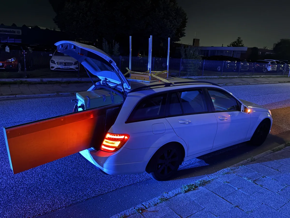 Ein weißer Kombi steht bei Nacht auf der Straße, die Heckklappe ist geöffnet und zeigt eine große Ladung im Kofferraum.