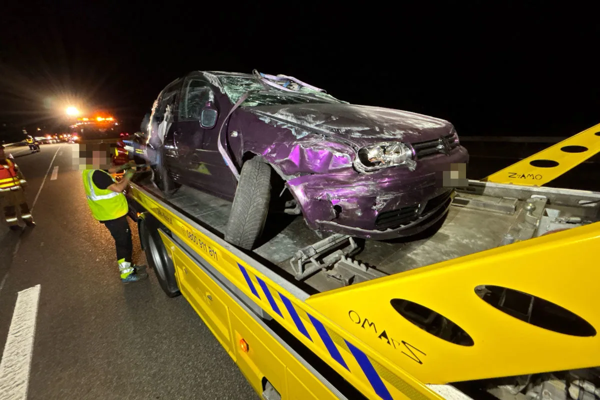 Ein violettes Auto mit sichtbaren Schäden wird bei Nacht von einem gelben Abschleppwagen auf einer Autobahn entfernt.