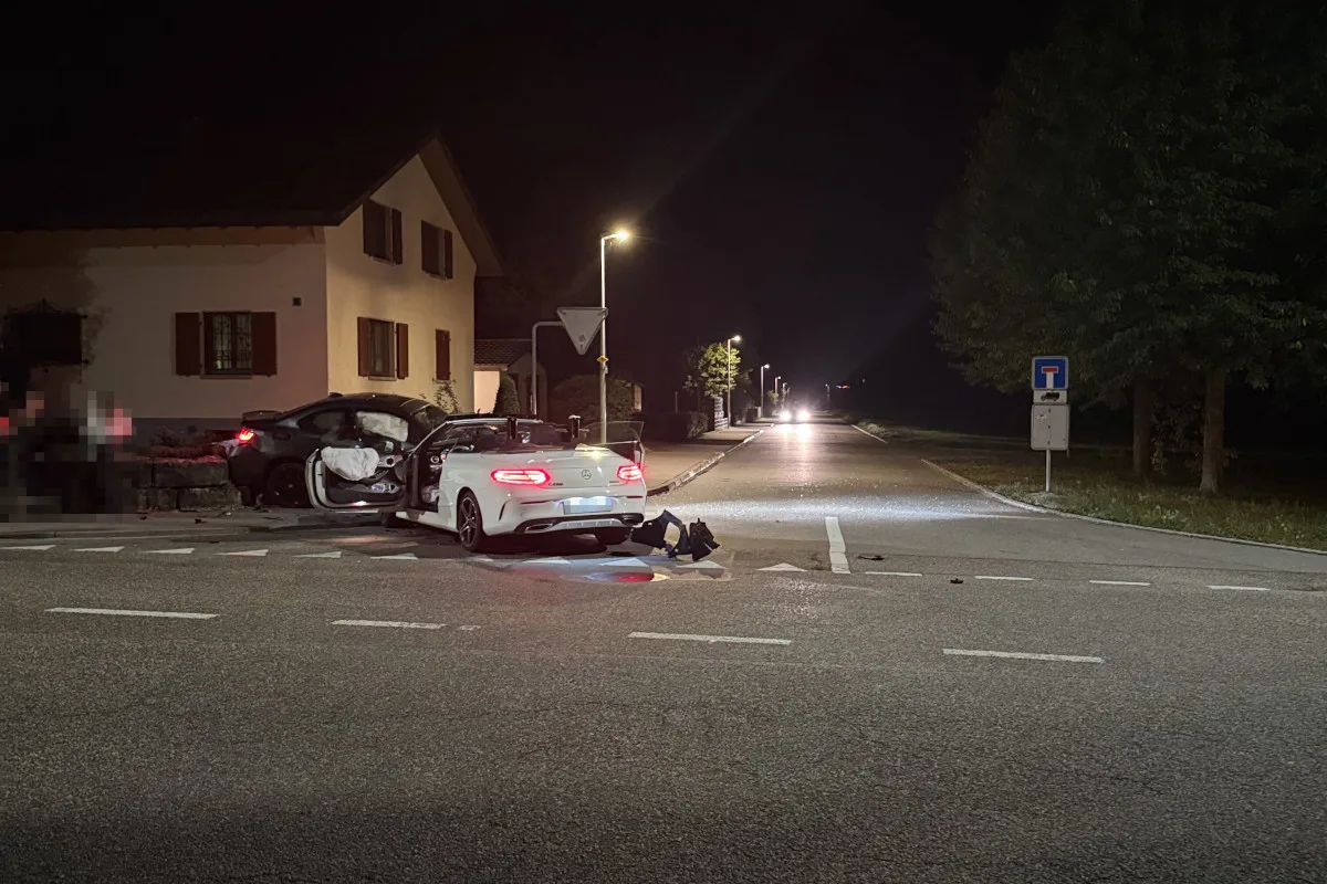 Zwei Fahrzeuge, eines weiß und eines schwarz, stehen beschädigt an einer Kreuzung. Es ist Nacht und die Straße ist beleuchtet.
