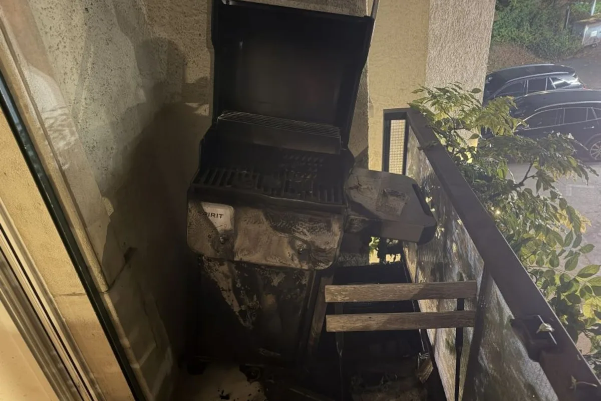 Auf einem Balkon steht ein beschädigter Grill mit sichtbaren Brandspuren an der Umgebung. Ein Stuhl zeigt ebenfalls leichte Brandschäden.