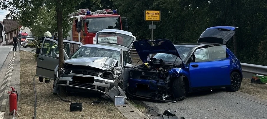 Zwei schwer beschädigte Autos stehen nach einem Unfall auf einer Landstraße, umgeben von Feuerwehr und Einsatzkräften.