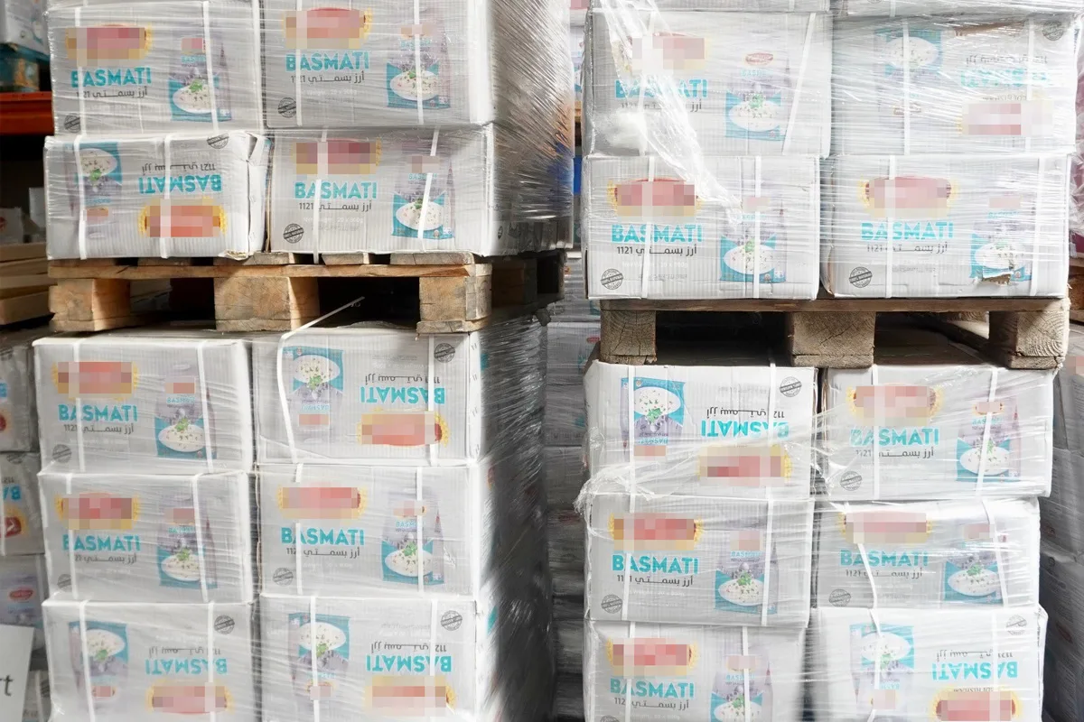 Mehrere gestapelte Packungen von Basmati-Reis sind auf Holzpaletten in einem Lagerraum zu sehen. Die Verpackungen sind in Plastikfolie gewickelt.