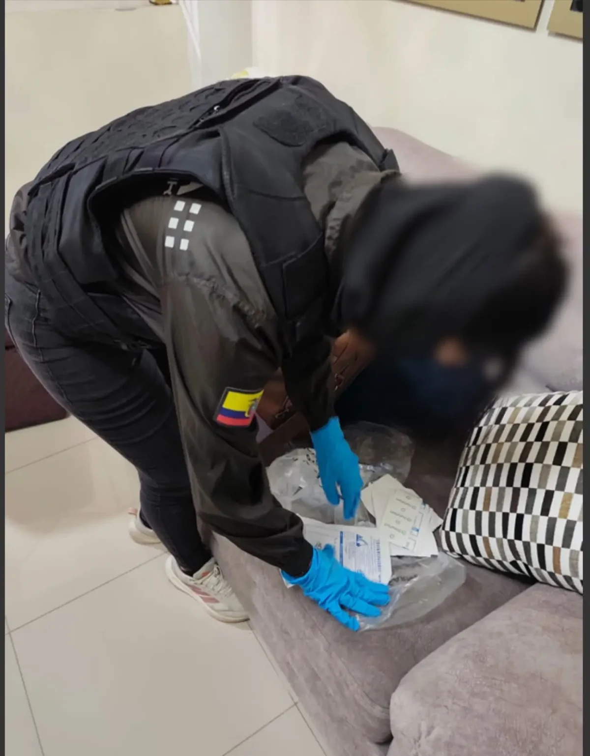 Eine Person in Uniform beugt sich über ein Sofa und untersucht Dokumente, während sie Handschuhe trägt.