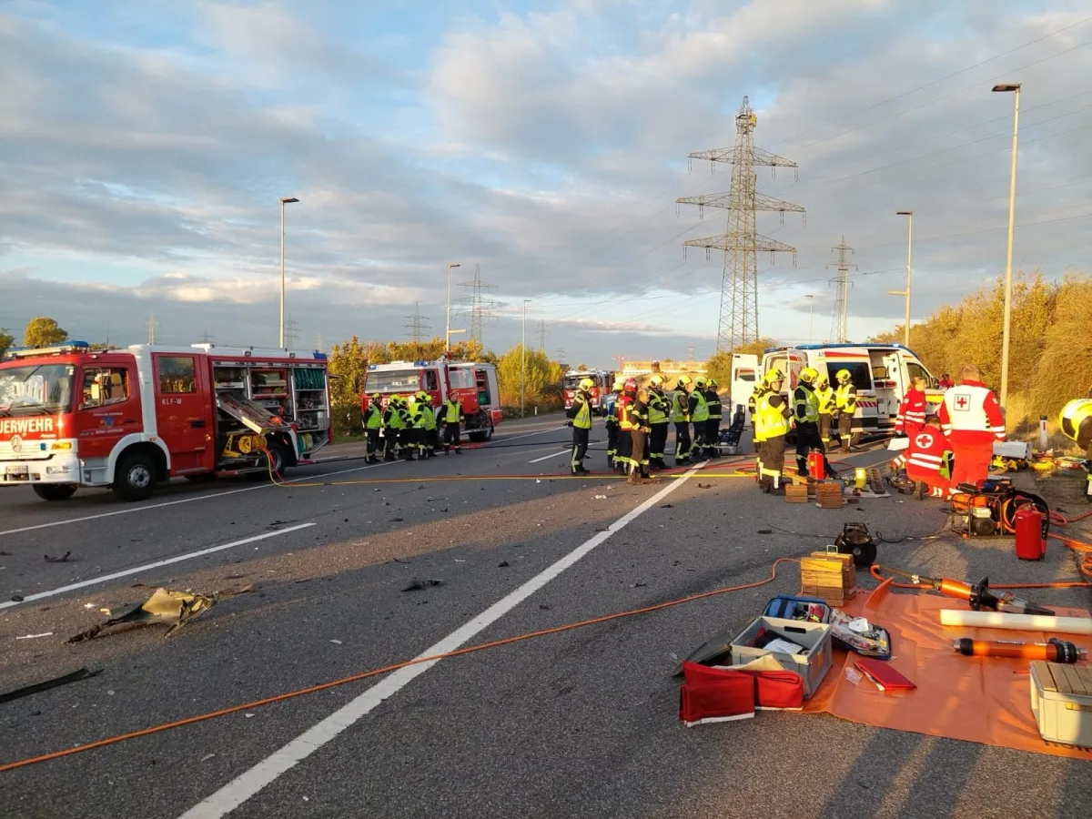 Einsatzkräfte sind auf einer Autobahn versammelt, umgeben von Feuerwehrfahrzeugen und Rettungsausrüstung. Trümmer liegen verstreut auf der Fahrbahn.