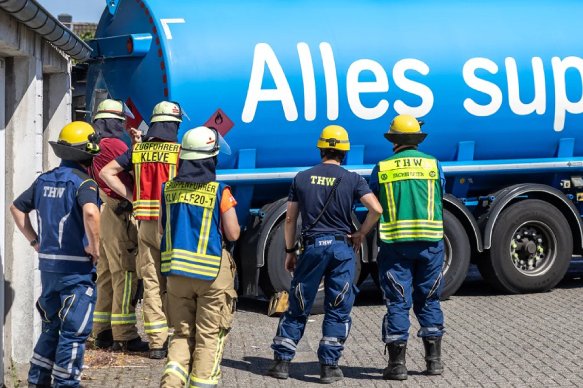 Mehrere THW-Einsatzkräfte stehen vor einem blauen Tankwagen mit aufgedrucktem Text. Sie tragen Helme und Schutzkleidung.