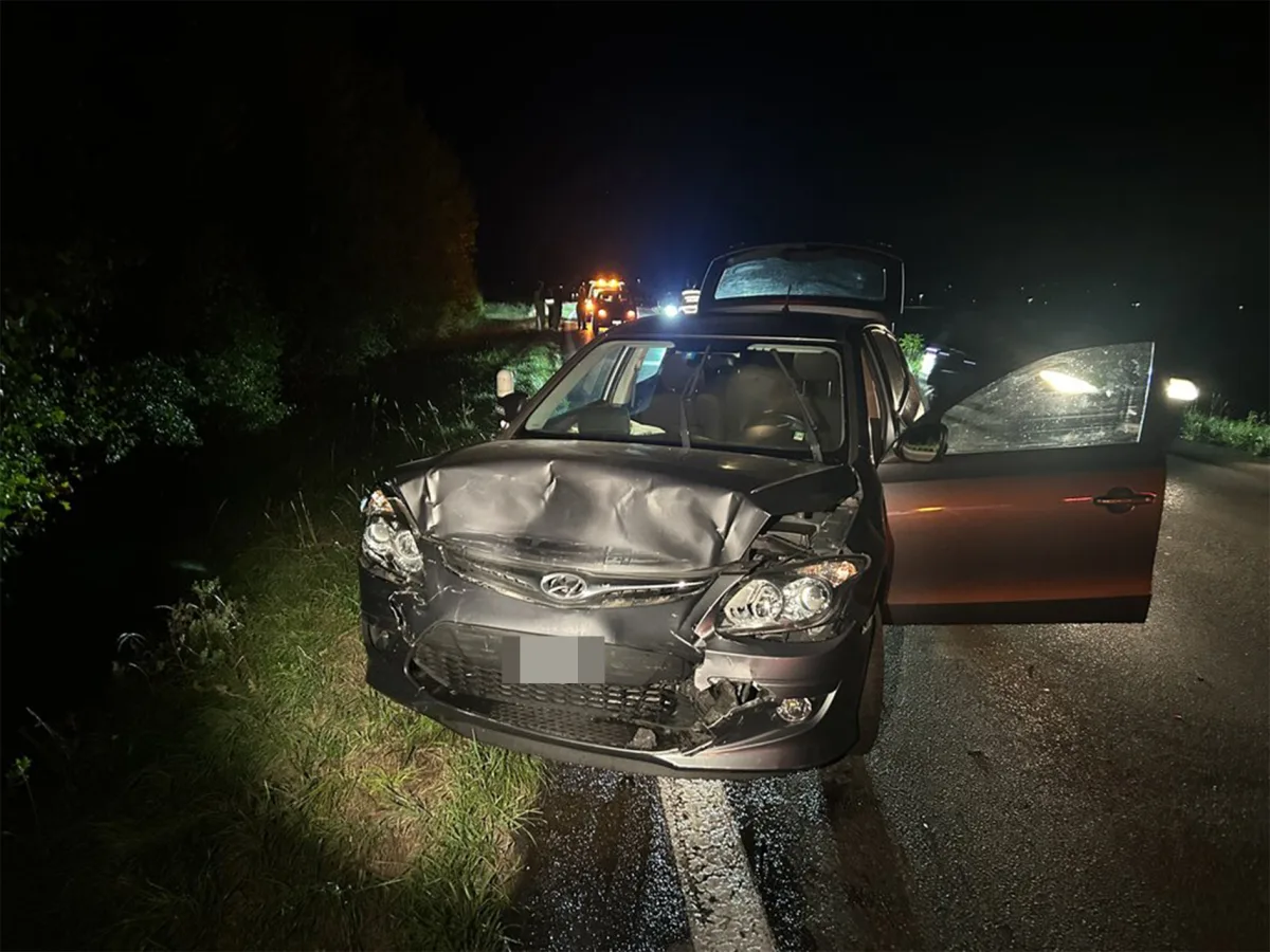 Ein Auto mit stark beschädigter Frontpartie steht auf einer Landstraße bei Nacht. Die Fahrertür ist geöffnet.