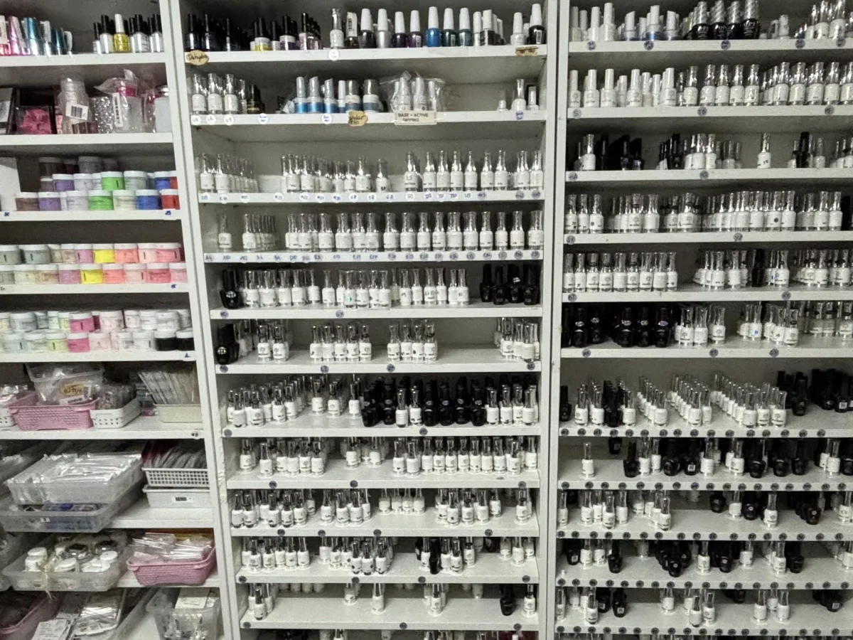 Mehrere Regale sind mit einer Vielzahl von Nagellackfläschchen und Zubehör bestückt. Die Produkte sind dicht an dicht aufgestellt.