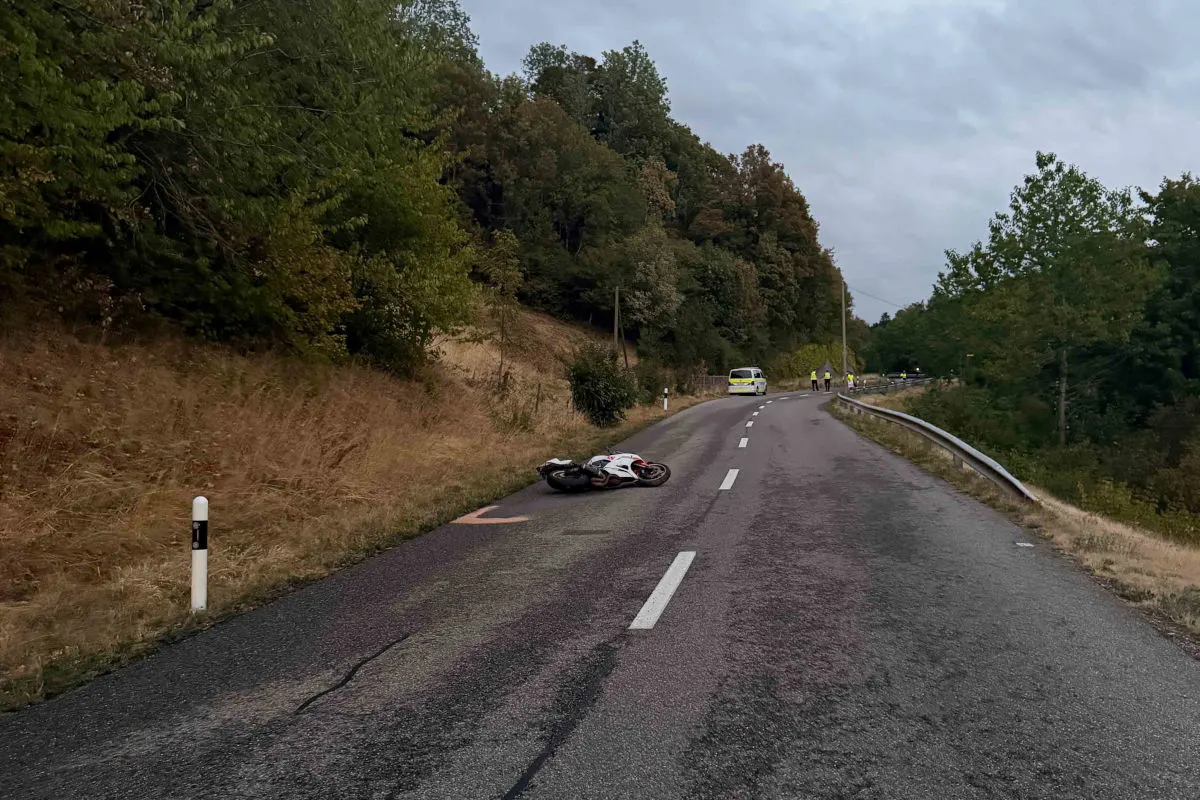 Auf einer kurvigen Landstraße liegt ein verunglücktes Motorrad. Im Hintergrund sichern Einsatzkräfte die Unfallstelle ab.