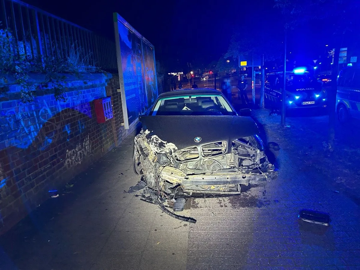 Ein stark beschädigtes Auto steht nachts auf einem Gehweg. Daneben sind Polizeifahrzeuge mit eingeschaltetem Blaulicht zu sehen.