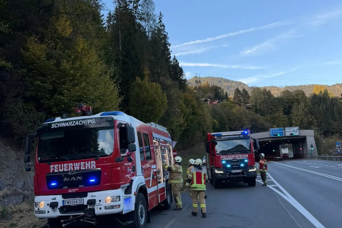 Zwei rote Feuerwehrfahrzeuge stehen auf einer Landstraße vor einem Tunnel; mehrere Feuerwehrleute sind sichtbar.