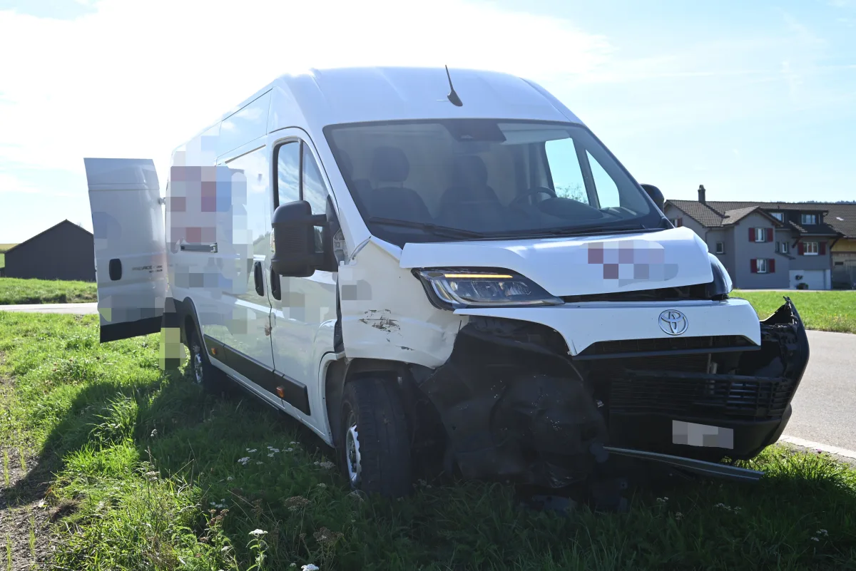 Ein weißer Transporter mit deutlichen Schäden an der Frontpartie steht am Straßenrand einer ländlichen Gegend. Die Fahrertür ist geöffnet.