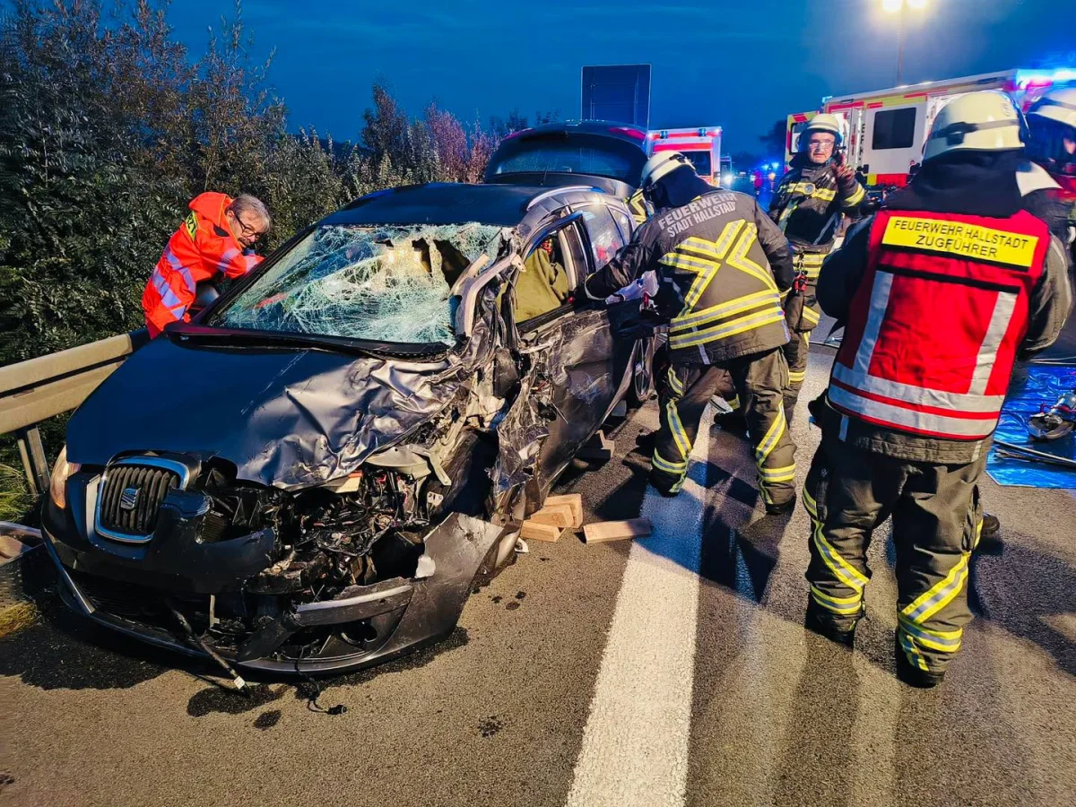 Mehrere Feuerwehrkräfte stehen um ein schwer beschädigtes Auto auf einer Straße. Das Fahrzeug zeigt deutliche Unfallschäden.