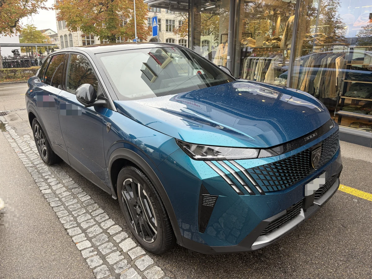 Ein blauer SUV steht auf dem Gehweg, direkt vor einem Schaufenster mit Kleidung. Der Wagen ist nass vom Regen.