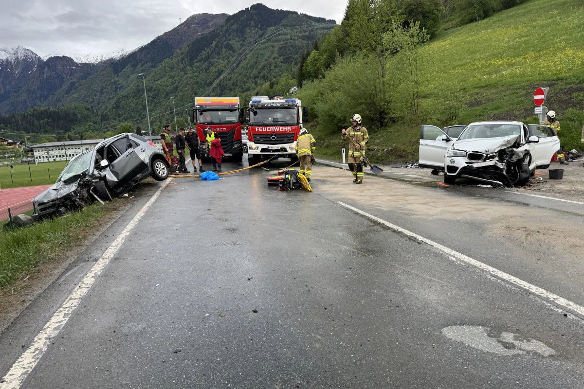 Auf einer Landstraße stehen zwei beschädigte Autos, ein silbernes links im Graben und ein weißes rechts. Ein Feuerwehrauto ist dazwischen positioniert, während Feuerwehrleute vor Ort sind.