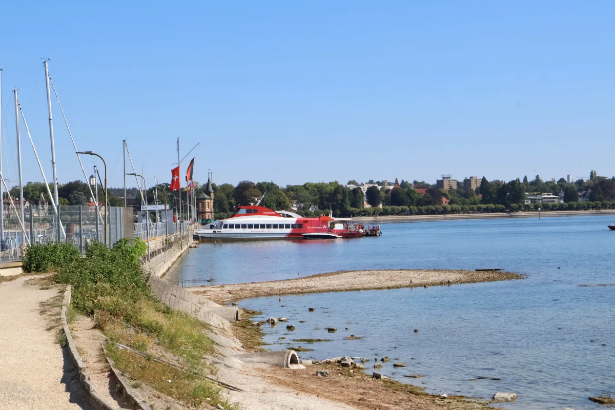 Ein rotes Passagierschiff ist an einem Pier festgemacht. Im Vordergrund wehen mehrere Flaggen, darunter die Schweizer Flagge.