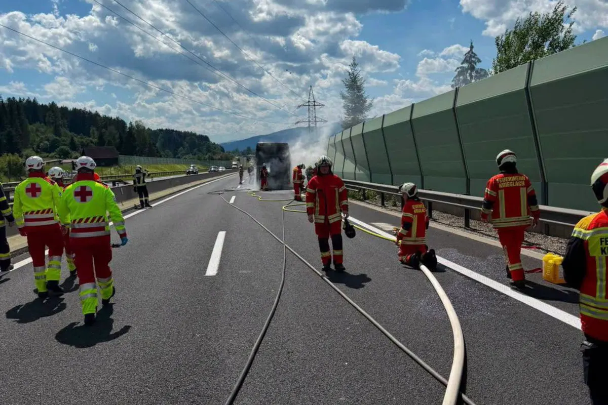 Mehrere Feuerwehrleute in Einsatzkleidung stehen auf einer Autobahn neben einem brennenden Bus. Rauch steigt aus dem Fahrzeug und Schläuche liegen auf der Fahrbahn.