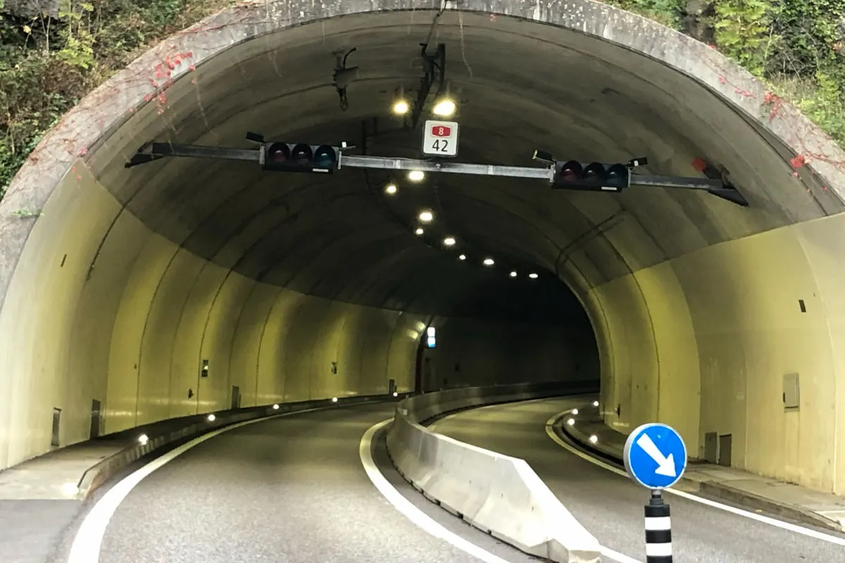 Ein Straßentunnel mit Ampelanlage über der Fahrbahn und blauem Verkehrsschild am Eingang. Die Straße ist in eine Richtung geöffnet.