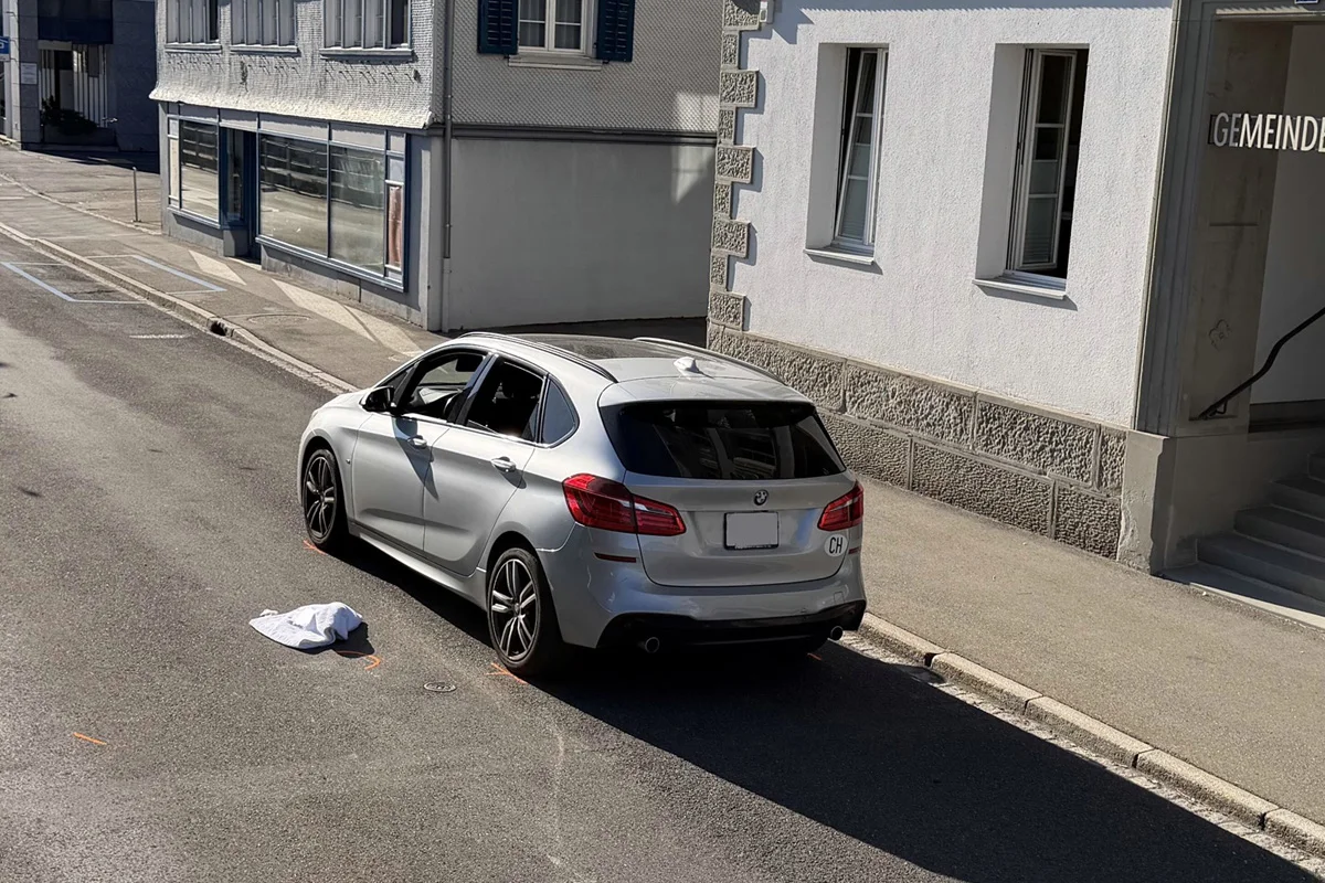 Ein silberner BMW steht am Straßenrand vor einem Gebäude, die Fensterscheiben des Fahrzeugs sind eingeschlagen. Auf der Straße liegt ein weißes Tuch.
