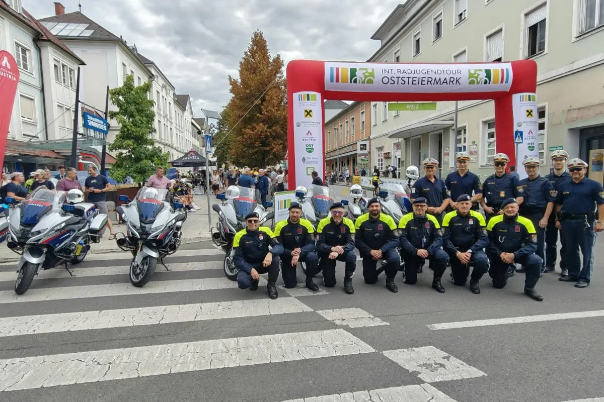 Eine Gruppe österreichischer Polizisten posiert vor Polizeimotorrädern. Im Hintergrund ist eine Veranstaltung mit Zuschauern zu sehen.