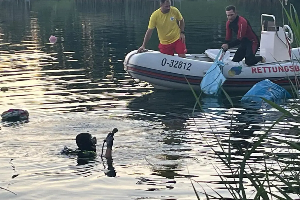 Ein Rettungsboot mit zwei Personen steht auf einem See, während ein Taucher daneben Gegenstände aus dem Wasser holt.