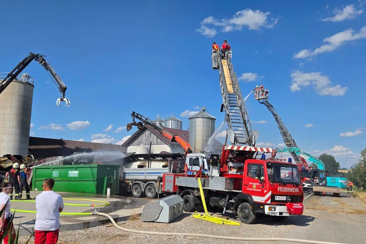 Mehrere Feuerwehrfahrzeuge sind dabei, einen Brand auf einem Hof zu löschen. Einsatzkräfte sind auf den Leiterwagen zu sehen.