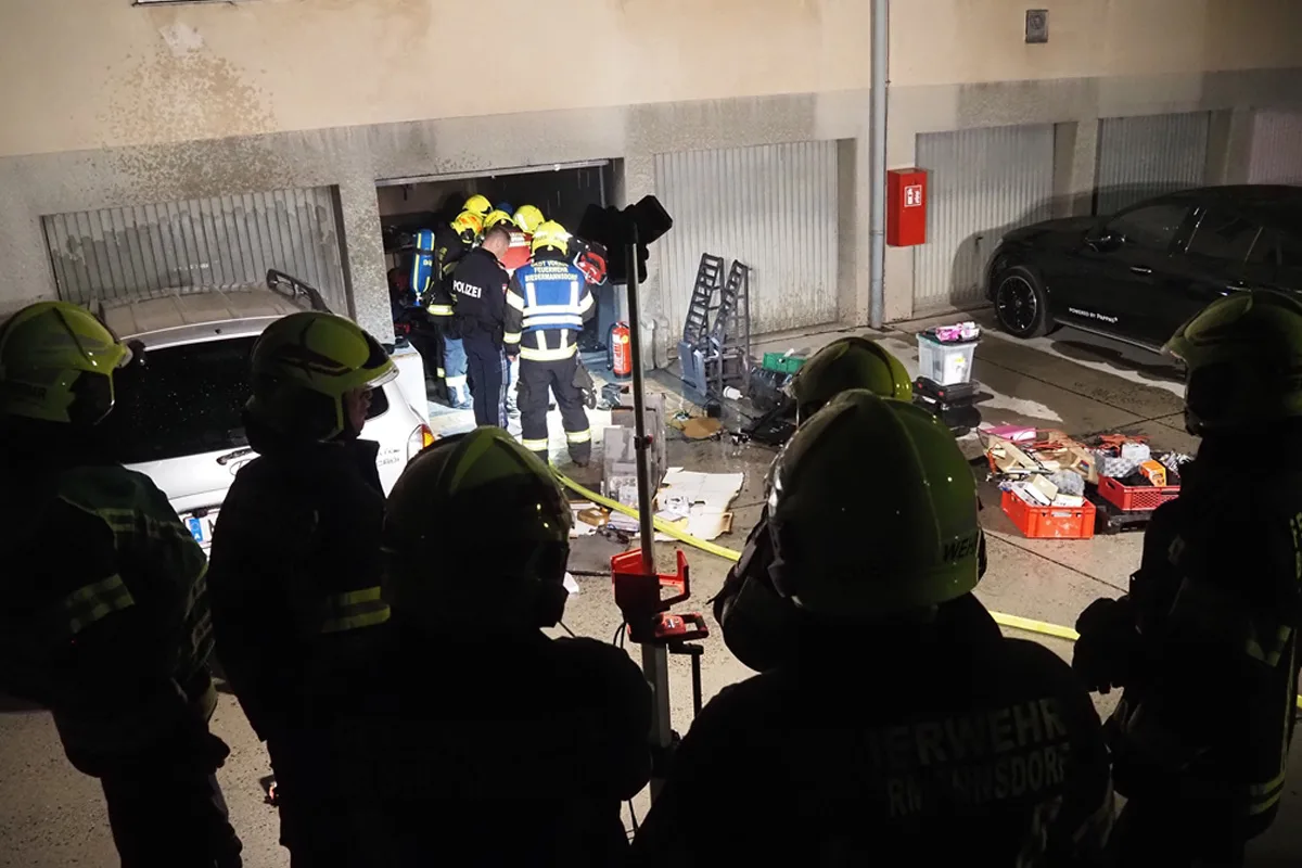 Mehrere Feuerwehr- und Polizeikräfte stehen in einer geöffneten Garage, die mit diversen Gegenständen gefüllt ist. Im Vordergrund sind die Umrisse von Einsatzkräften zu erkennen.