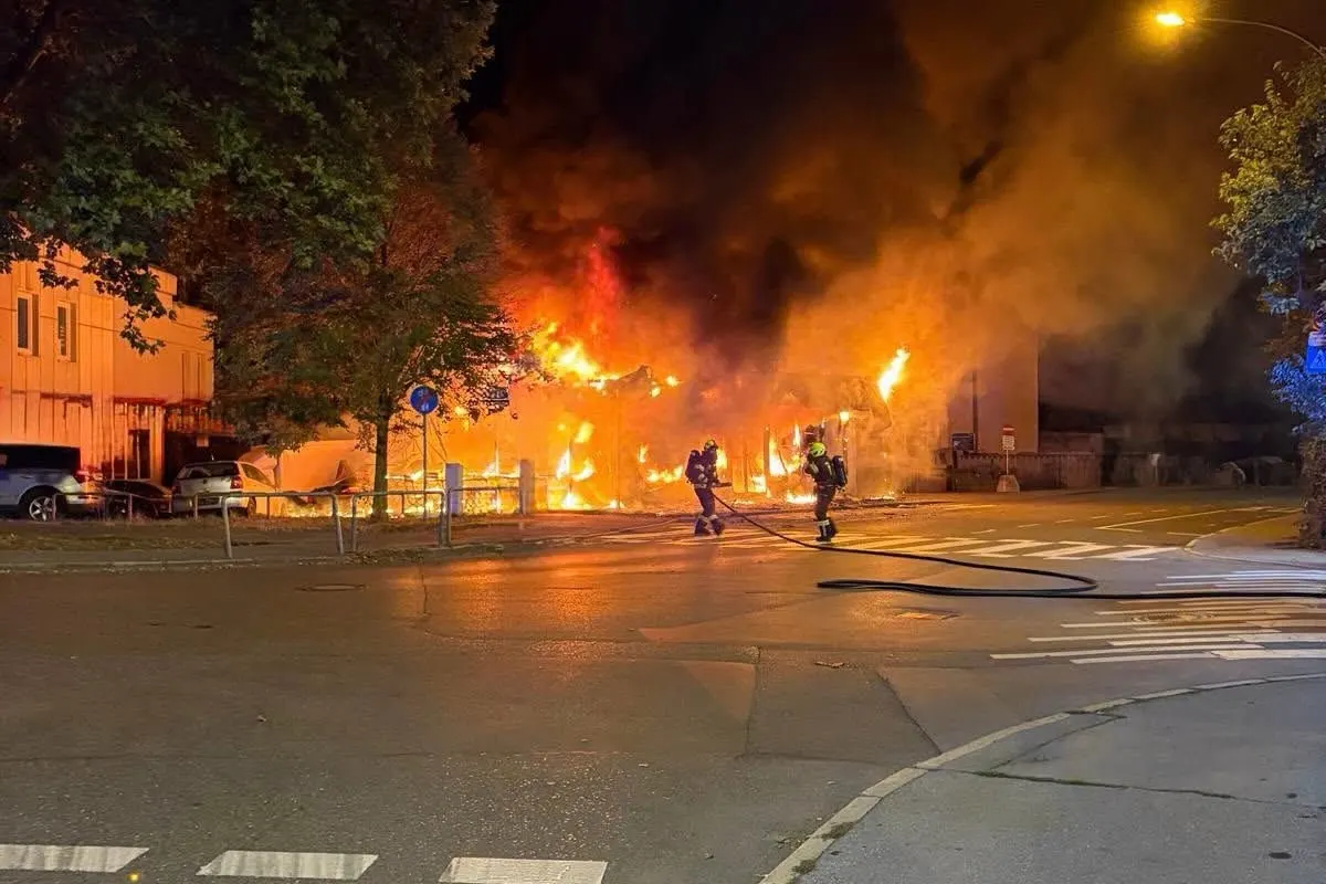 Bei Nacht löschen Feuerwehrleute einen großflächigen Brand in einem Gebäude. Flammen schlagen in den Himmel.