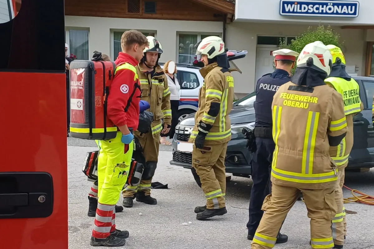 Mehrere Einsatzkräfte der Feuerwehr und Polizei stehen vor einem Gebäude und scheinen eine Lagebesprechung abzuhalten. Im Hintergrund ist ein Polizeiauto zu sehen.