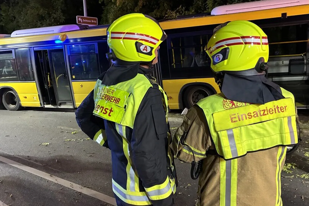 Zwei Feuerwehrleute in gelber Schutzkleidung stehen vor einem gelben Bus. Die Szene findet nachts oder abends statt.