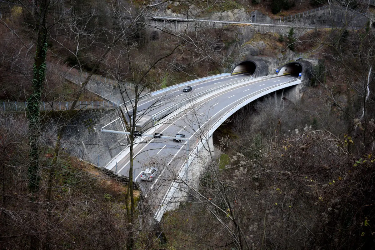 Eine Straße führt über eine Brücke und in zwei Tunnel, umgeben von kahlen Bäumen und Hügeln.