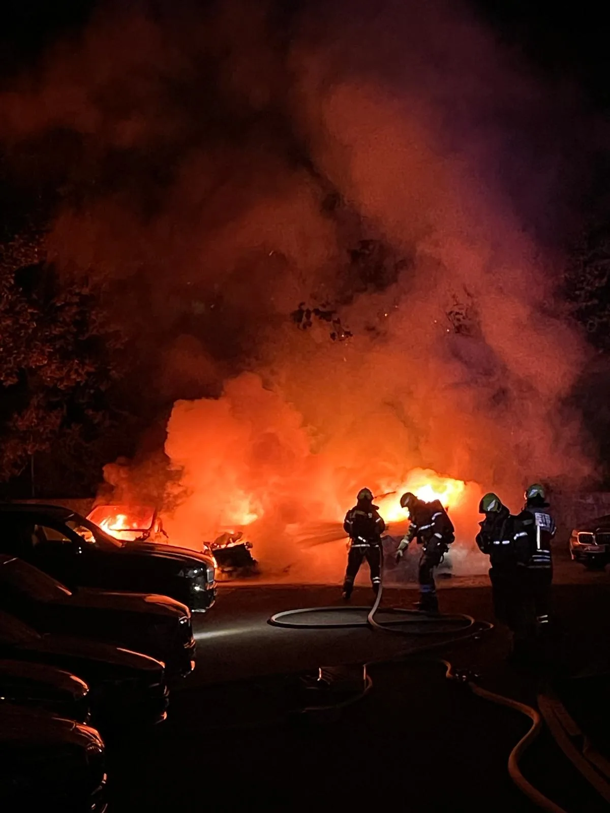 Mehrere Feuerwehrleute sind bei Nacht im Einsatz, um ein brennendes Auto zu löschen. Das Fahrzeug steht unter dichter Rauchentwicklung in Flammen.