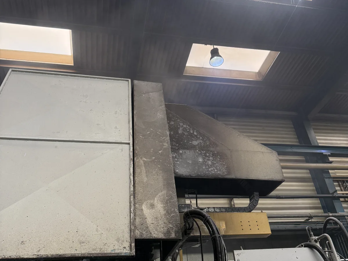 Eine große Industriemaschine befindet sich in einer Fabrikhalle. Oberlichter erhellen die Szene von oben.