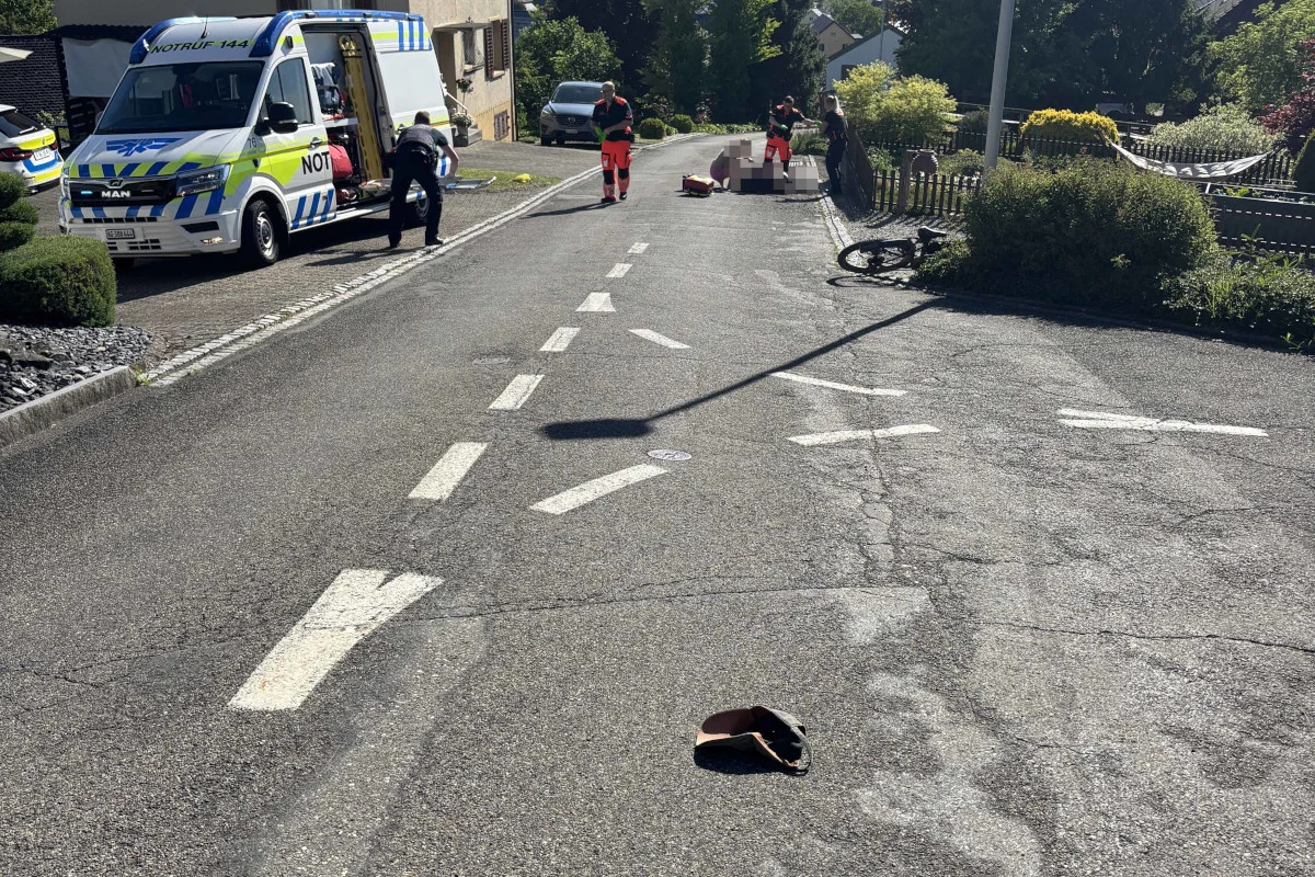 Ein Rettungswagen steht auf einer Straße, während Sanitäter eine Person versorgen. Ein Fahrrad liegt am Straßenrand.