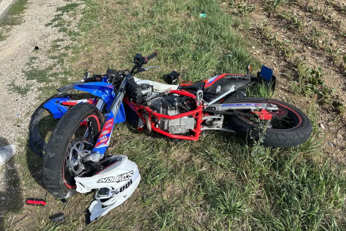 Ein blau-rotes Motorrad liegt stark beschädigt im Gras neben einer Straße. Der Vorderreifen und der Rahmen zeigen deutliche Schäden.