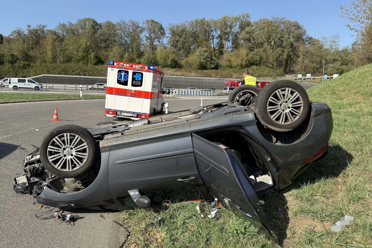 Ein Auto ist auf einer Straße auf dem Dach gelandet. Im Hintergrund steht ein Rettungswagen mit Ambulanz-Aufschrift.
