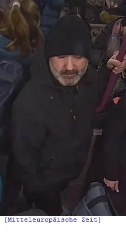 Ein Mann mit Bart, der eine dunkle Jacke und Mütze trägt, steht in einer vollen Menschenmenge.
