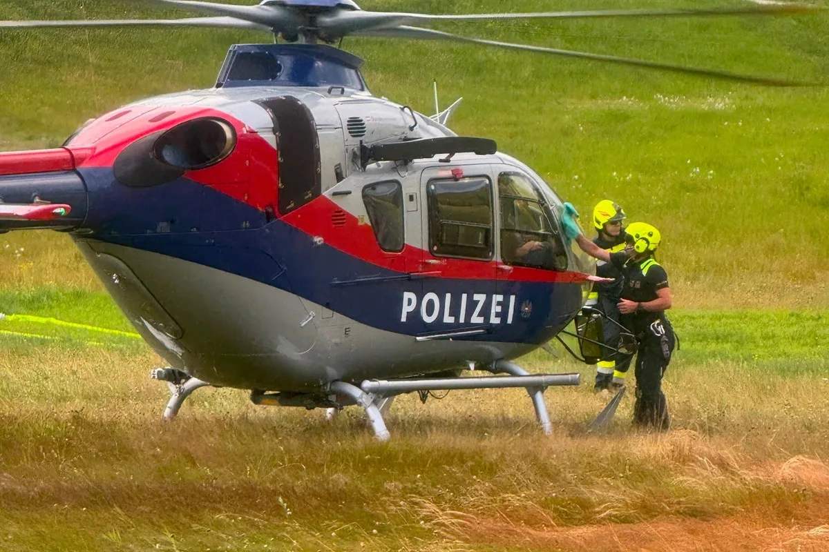 Ein Polizeihubschrauber steht auf einer Wiese, umgeben von mehreren Einsatzkräften in gelben Helmen.