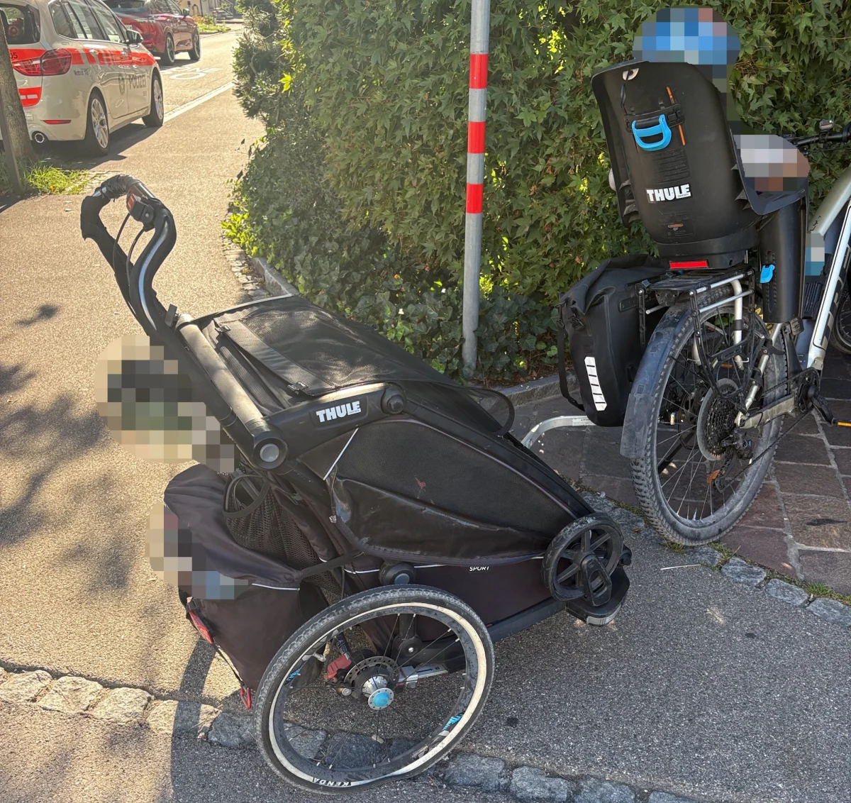 Ein Fahrrad mit Kindersitz und ein Fahrradanhänger stehen auf einem Gehweg, im Hintergrund ein Polizeifahrzeug.