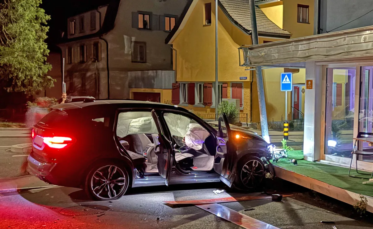 Ein schwarzes Auto steht mit geöffneten Türen und ausgelösten Airbags auf dem Gehweg vor einem Gebäude. Der Unfall geschah nachts.
