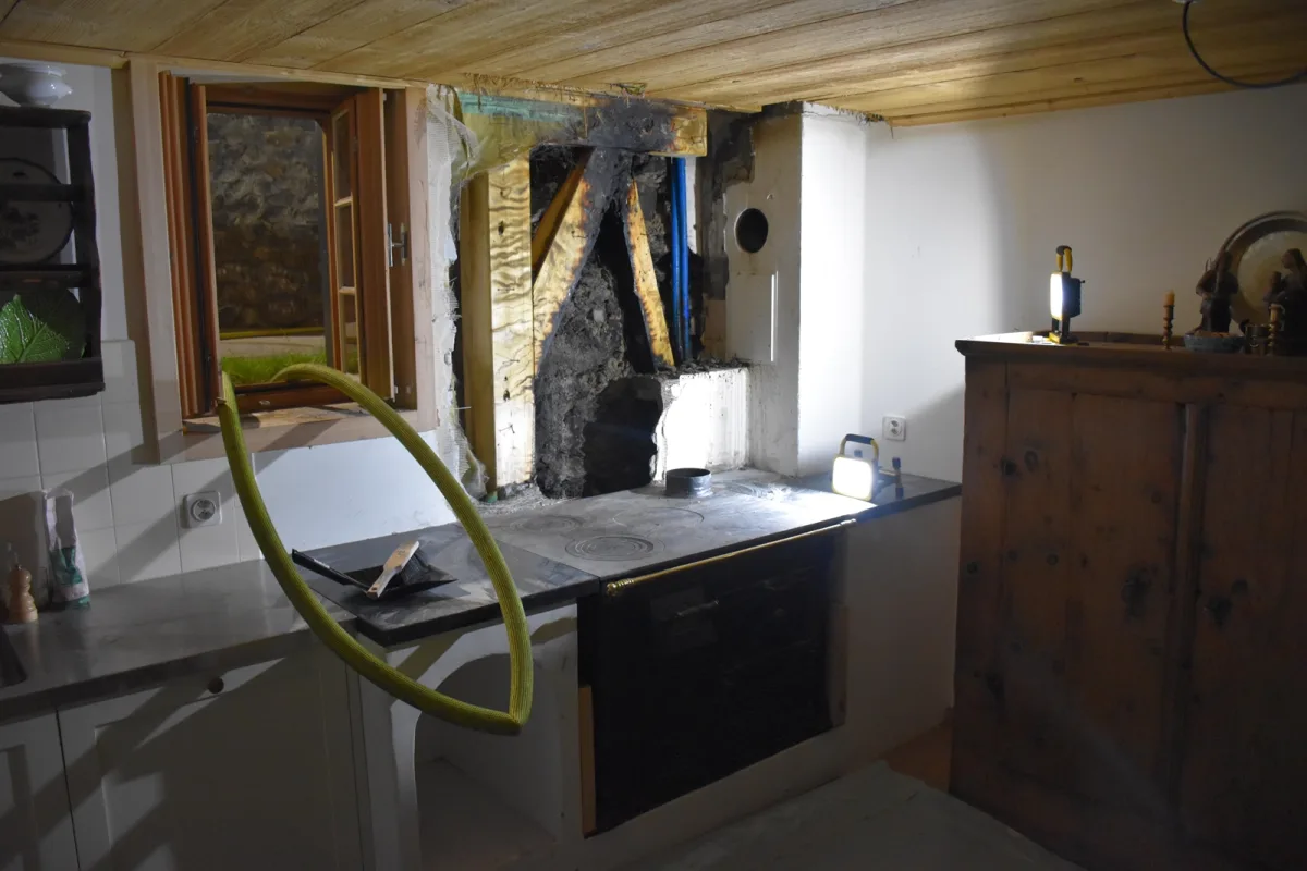 Ein Raum mit sichtbarer Beschädigung an der Küchenwand durch Ruß. Ein Fenster ist offen, Licht fällt auf die Arbeitsfläche.